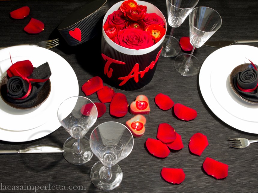 Tavola apparecchiata con runner nero, petali di rosa rossi e una Flower Box con Rose e Ranuncoli rossi