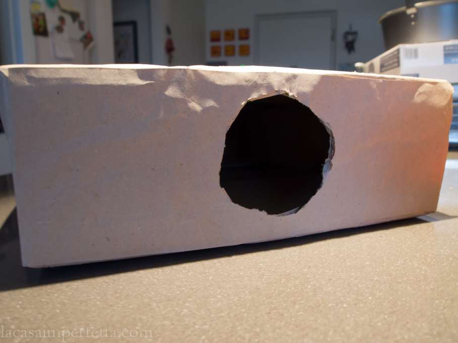 Fase di creazione della mistery box a forma di libro. Scatola chiusa con fori laterali e rivestita da carta da pacco marroncina