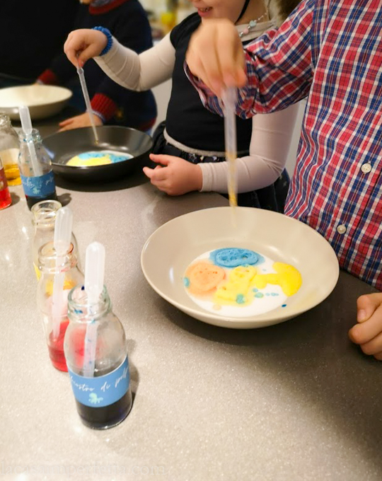 Bambini che giocano con le boccette di vetro con colore alimentare e aceto; piatto con bicarbonato e pipette di plastica