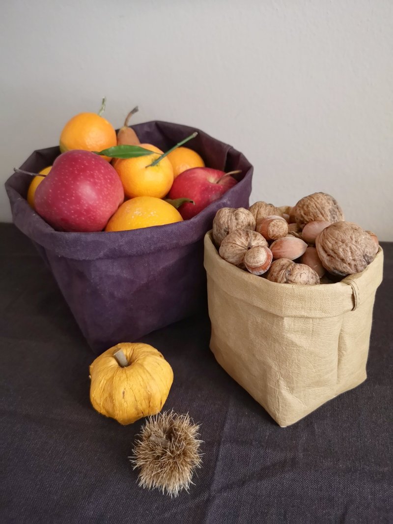 Due cestini porta frutta: uno viola con mele, mandarini e pere; uno piccolo color tabaccon con noci e nocciole nel guscio