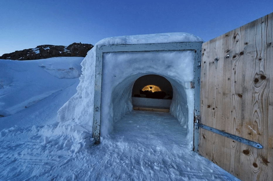 Ingresso dell'igloo con la porta aperta da dove si intravede il letto alla luce delle candele